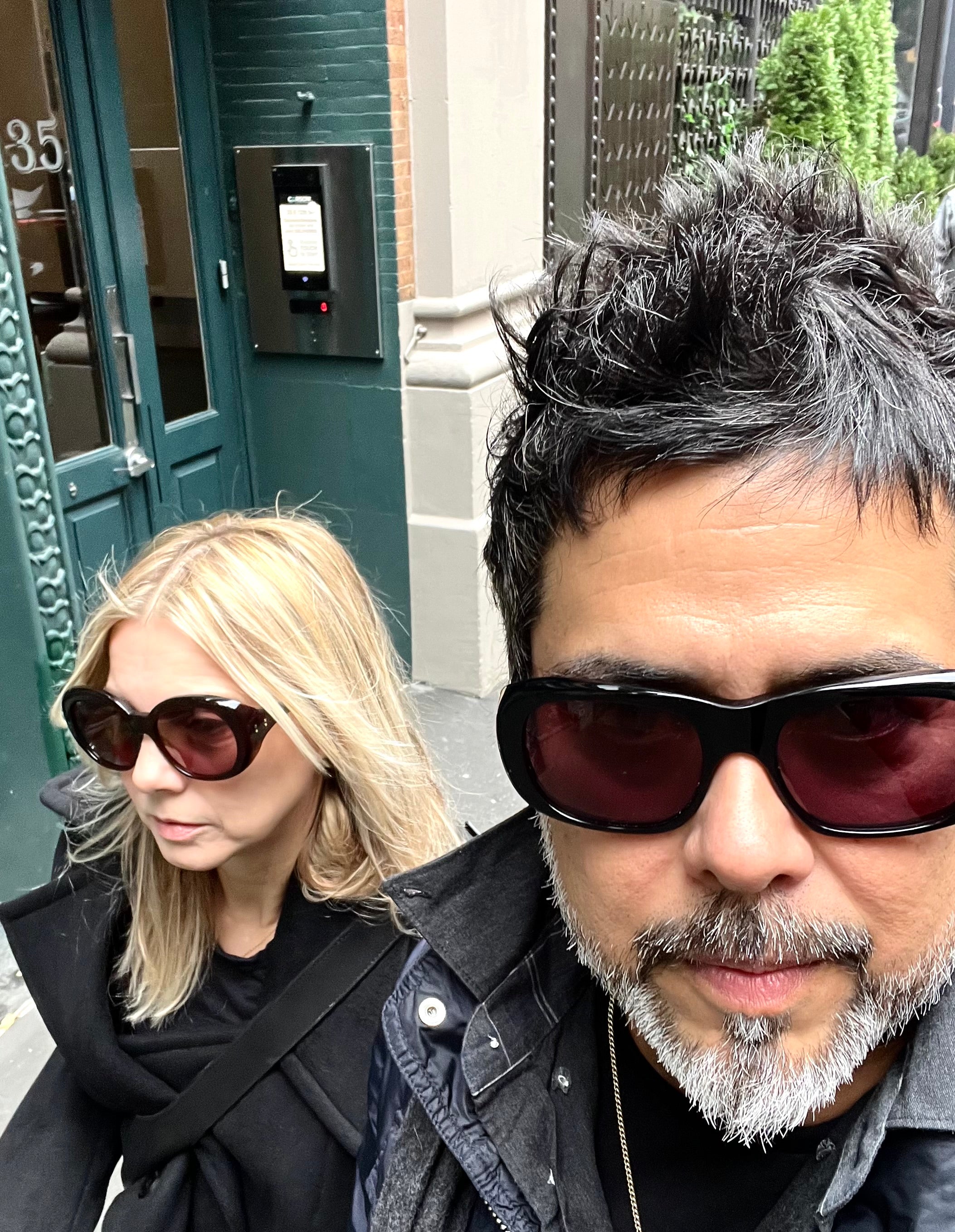 Two people wearing sunglasses with a building and door in the background